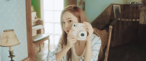 A Woman Is Taking A Picture Of Herself With A White Camera . GIF