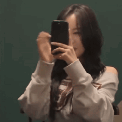 A Woman Is Taking A Picture Of Herself With Her Phone . GIF