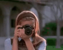 A Woman Is Taking A Picture With A Camera And Smiling . GIF