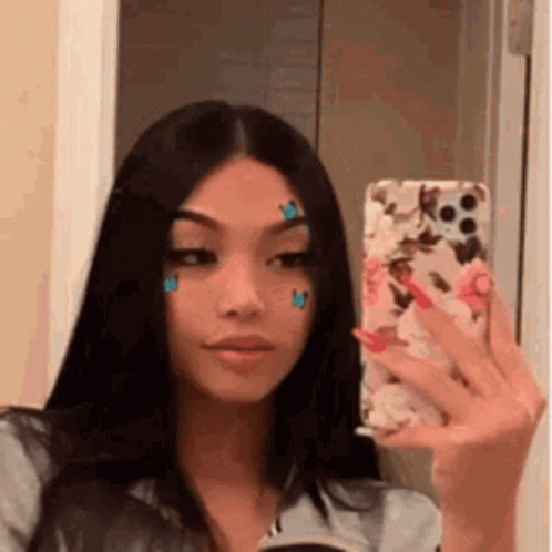 A Woman Is Taking A Selfie In Front Of A Mirror With A Cell Phone . GIF