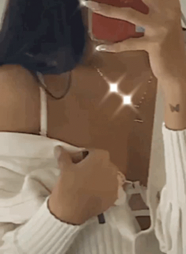 A Woman Is Taking A Selfie In Front Of A Mirror With Her Phone . GIF