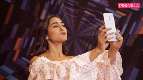A Woman Is Taking A Selfie In Front Of A Pinkvilla Banner GIF