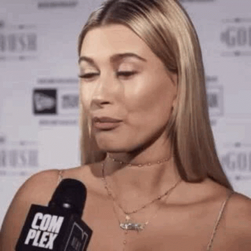 A Woman Is Talking Into A Microphone While Wearing A Choker Necklace . GIF