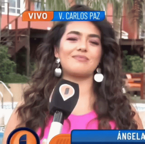 A Woman Is Talking Into A Microphone With A Banner Above Her That Says Vivo V. Carlos Paz GIF