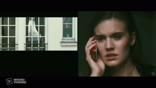 A Woman Is Talking On A Cell Phone In Front Of A Window With Russian Writing On The Bottom GIF