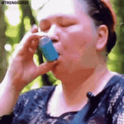 A Woman Is Talking On A Cell Phone While Holding A Blue Asthma Inhaler In Her Mouth . GIF