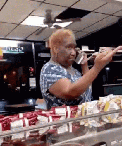 A Woman Is Talking On A Cell Phone While Standing In Front Of A Counter . GIF