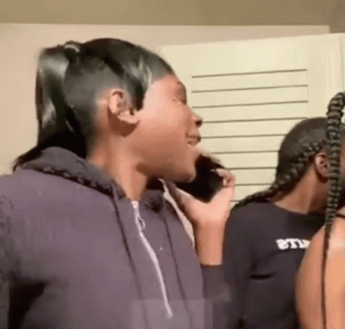 A Woman Is Talking On A Cell Phone While Standing Next To Another Woman In A Room . GIF