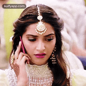 A Woman Is Talking On A Cell Phone While Wearing A Headpiece And Earrings . GIF