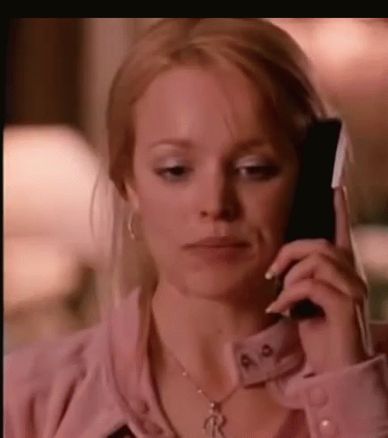 A Woman Is Talking On A Cell Phone While Wearing A Pink Shirt And A Necklace . GIF