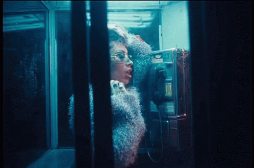 A Woman Is Talking On A Pay Phone In A Booth GIF