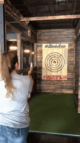 A Woman Is Throwing An Axe At A Target That Has #Badaxe Written On It GIF