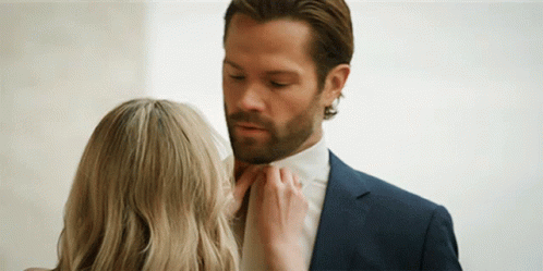 A Woman Is Touching A Man 'S Tie While He Is Wearing A Suit And Tie . GIF