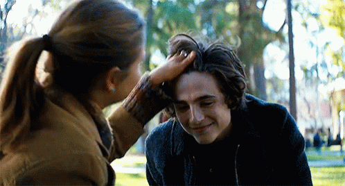 A Woman Is Touching A Young Man 'S Head In A Park . GIF