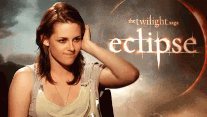 A Woman Is Touching Her Hair In Front Of A Poster For The Twilight Saga Eclipse . GIF