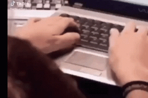 A Woman Is Typing On A Laptop Computer While Holding A Mouse . GIF