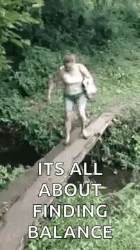 A Woman Is Walking Across A Small Wooden Bridge Over A Stream . GIF