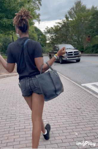 A Woman Is Walking Down A Brick Sidewalk With A Dodge Truck In The Background And The Word Imgplay At The Bottom GIF
