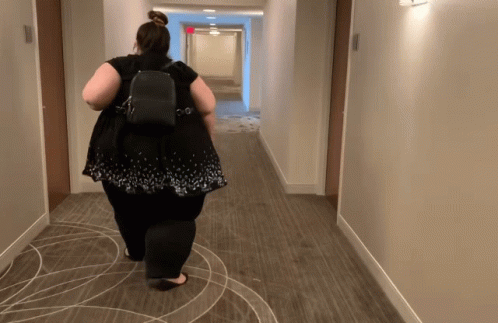 A Woman Is Walking Down A Hallway With A Backpack GIF
