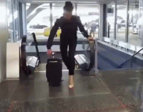 A Woman Is Walking Down A Hallway With A Suitcase On Her Feet GIF