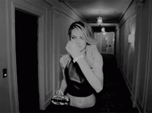 A Woman Is Walking Down A Hallway With Her Hand On Her Face GIF
