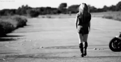 A Woman Is Walking Down A Road In Front Of A Motorcycle . GIF