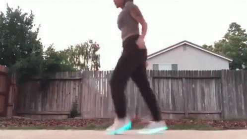 A Woman Is Walking Down A Sidewalk In Front Of A Fence And A House . GIF