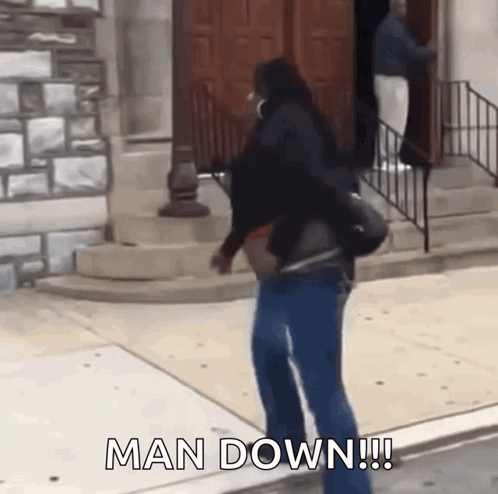 A Woman Is Walking Down A Sidewalk With The Words Man Down Written On The Ground . GIF