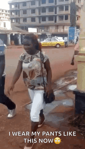 A Woman Is Walking Down A Street Wearing White Pants And A Shirt . GIF