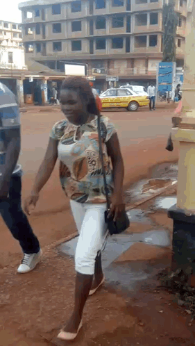 a woman is walking down a street with a yellow taxi behind her .