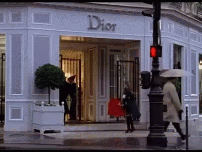 A Woman Is Walking In Front Of A Dior Store . GIF