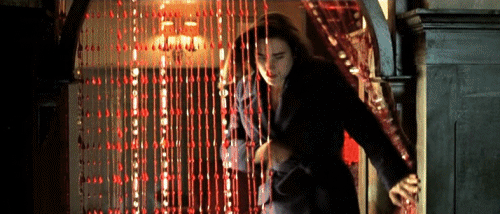 A Woman Is Walking Through A Doorway With A Red Curtain Behind Her . GIF