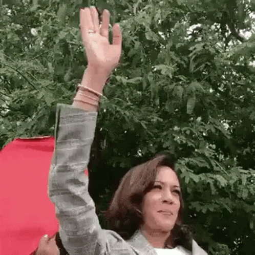 A Woman Is Waving Her Hand In Front Of A Tree . GIF