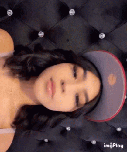 A Woman Is Wearing A Baseball Cap And Laying On A Bed . GIF