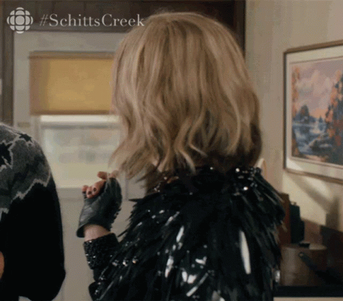 A Woman Is Wearing A Black Jacket And Gloves With #Schitts Creek On The Bottom GIF