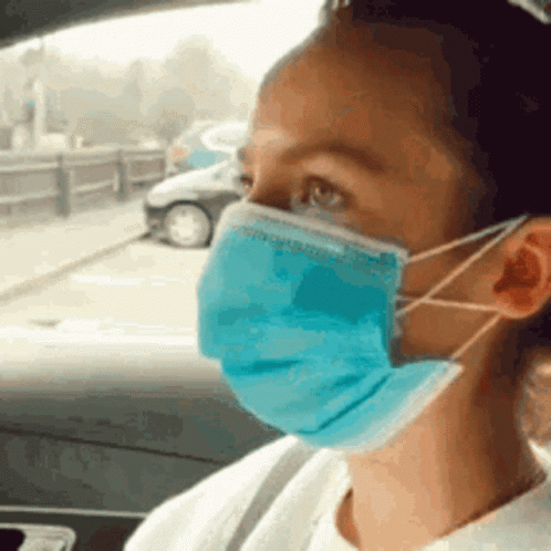 A Woman Is Wearing A Blue Face Mask While Sitting In A Car . GIF