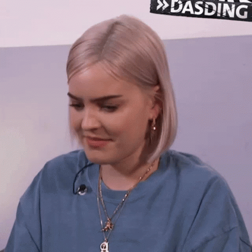 A Woman Is Wearing A Blue Shirt And A Necklace With A Letter A On It GIF