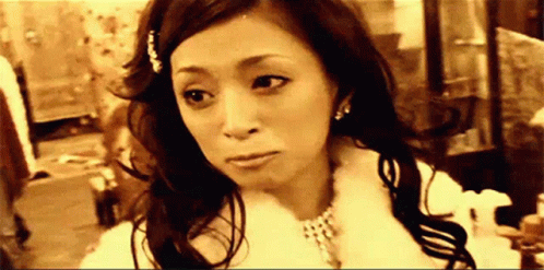 A Woman Is Wearing A Fur Coat And A Necklace And Looking At The Camera . GIF