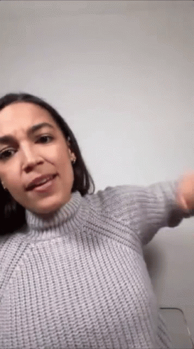 A Woman Is Wearing A Gray Sweater And Making A Funny Face . GIF
