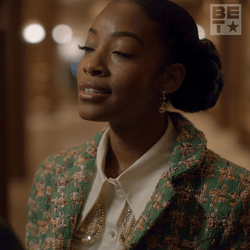 A Woman Is Wearing A Green Jacket And A White Shirt With A Be Logo In The Background GIF