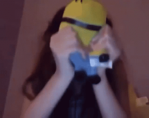 A Woman Is Wearing A Minion Mask And Holding A Camera GIF