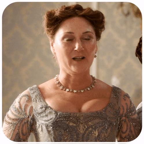 A Woman Is Wearing A Necklace And Earrings And A Gray Dress GIF