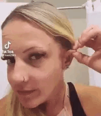 A Woman Is Wearing A Nose Ring And A Nose Ring While Holding Her Hair . GIF