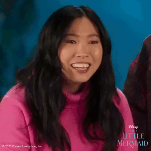 A Woman Is Wearing A Pink Sweater And Smiling For The Little Mermaid GIF