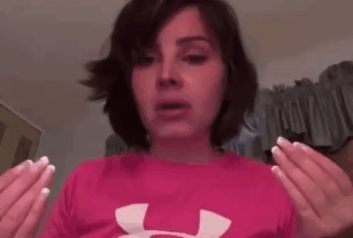 A Woman Is Wearing A Pink Under Armour Shirt And Holding Her Hands Up In The Air . GIF