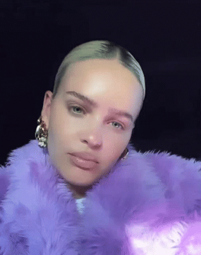 A Woman Is Wearing A Purple Fur Coat And Earrings . GIF