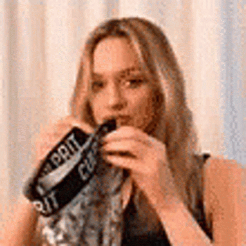 A Woman Is Wearing A Scarf Around Her Neck And Holding A Bottle Of Soda . GIF