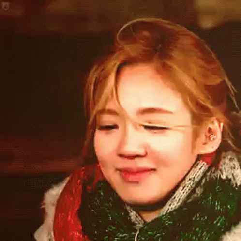 A Woman Is Wearing A Scarf Around Her Neck And Smiling . GIF