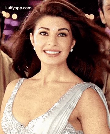 A Woman Is Wearing A Silver Dress And Smiling . GIF