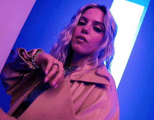 A Woman Is Wearing A Trench Coat And A Necklace GIF